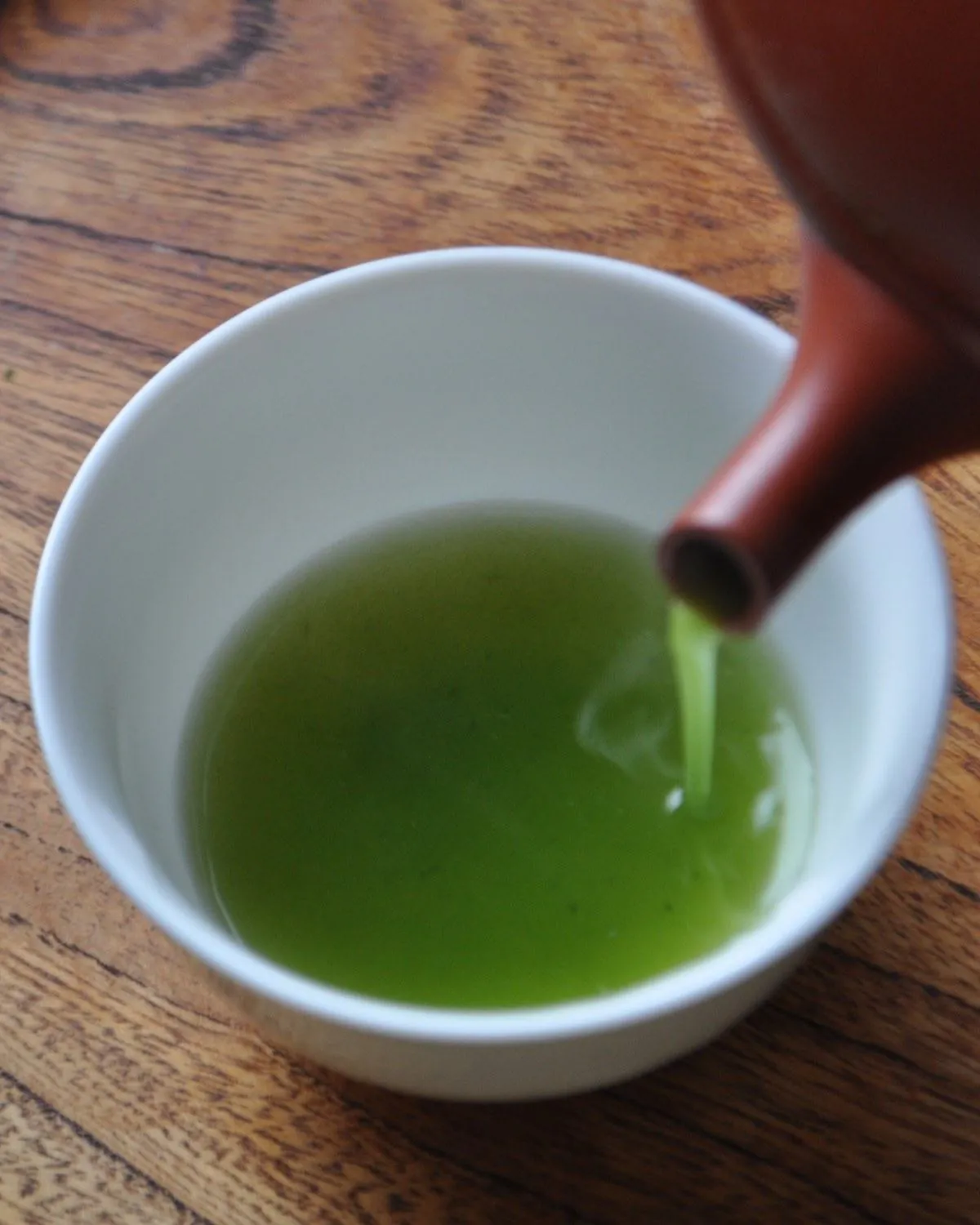 Pouring Chiran Asatsuyu sencha from a kyusu teapot into a porcelain cup — vivid emerald liquor