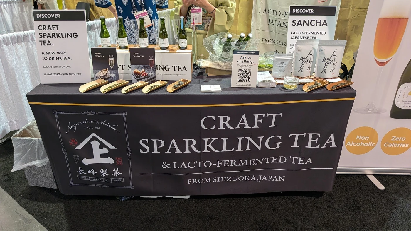 Nagamine Seicha booth at World Tea Expo 2026 Las Vegas — three craft sparkling tea bottles, Bodai-Sancha Powder, and tea leaf samples displayed on a dark booth table reading CRAFT SPARKLING TEA & LACTO-FERMENTED TEA — FROM SHIZUOKA, JAPAN
